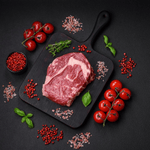 A raw beef roast on a black cutting board, flanked by cherry tomatoes and seasonings, against a black background.